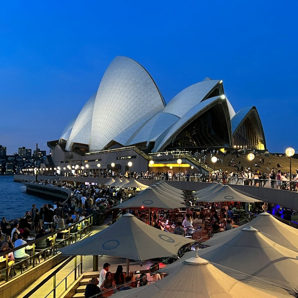 a large crowd of people at a concert with Sydney Opera House in the background